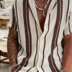 A man wearing a striped linen short-sleeved shirt and layered necklaces.