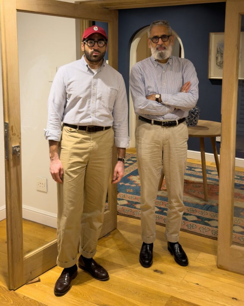 Two men posing in button-down shirts and khaki chino pants indoors.