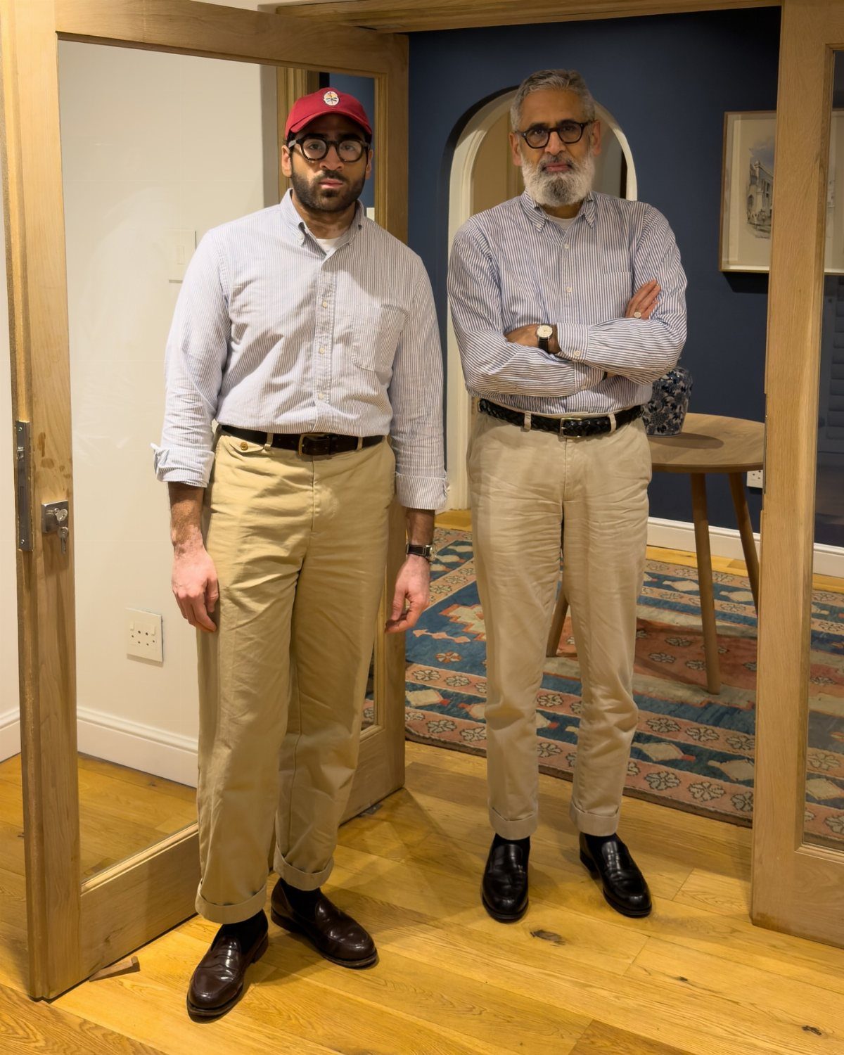Two men posing in button-down shirts and khaki chino pants indoors.