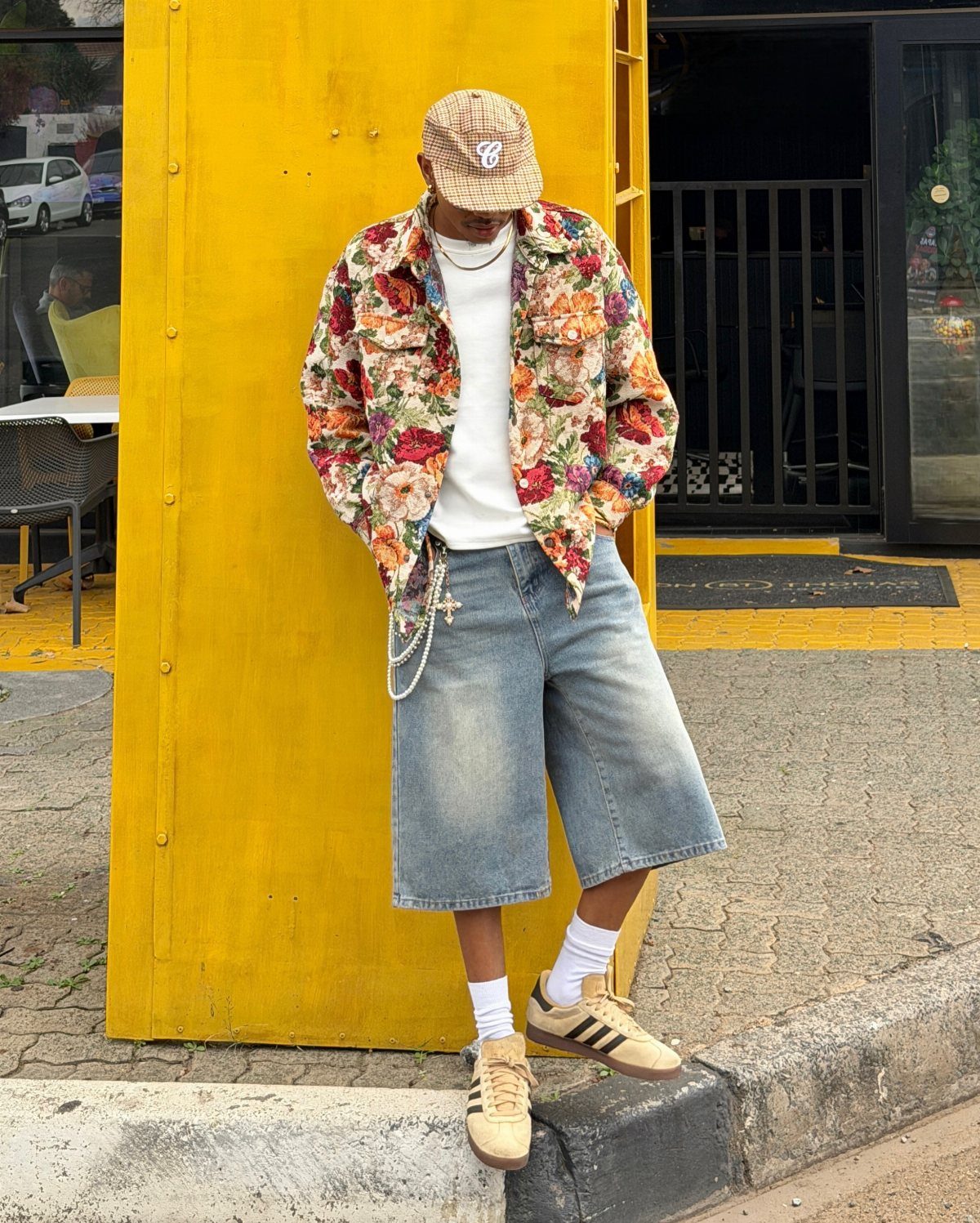 A person wearing a vibrant floral shirt, denim shorts, and a patterned bucket hat.