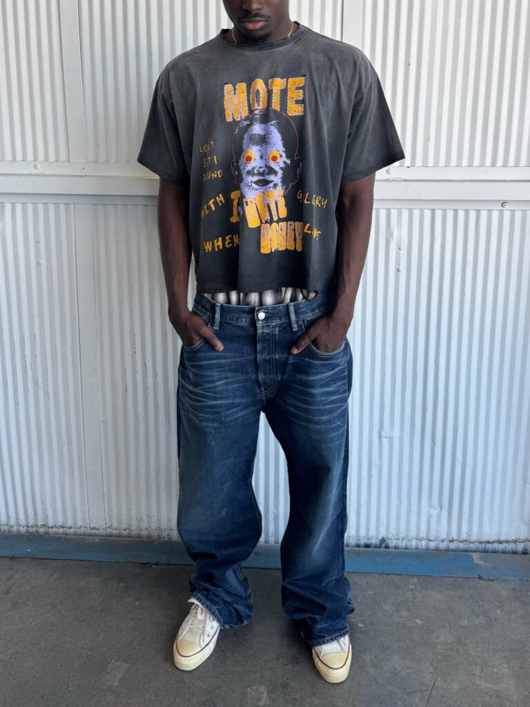 Person wearing a dark graphic t-shirt and baggy blue jeans with white sneakers.