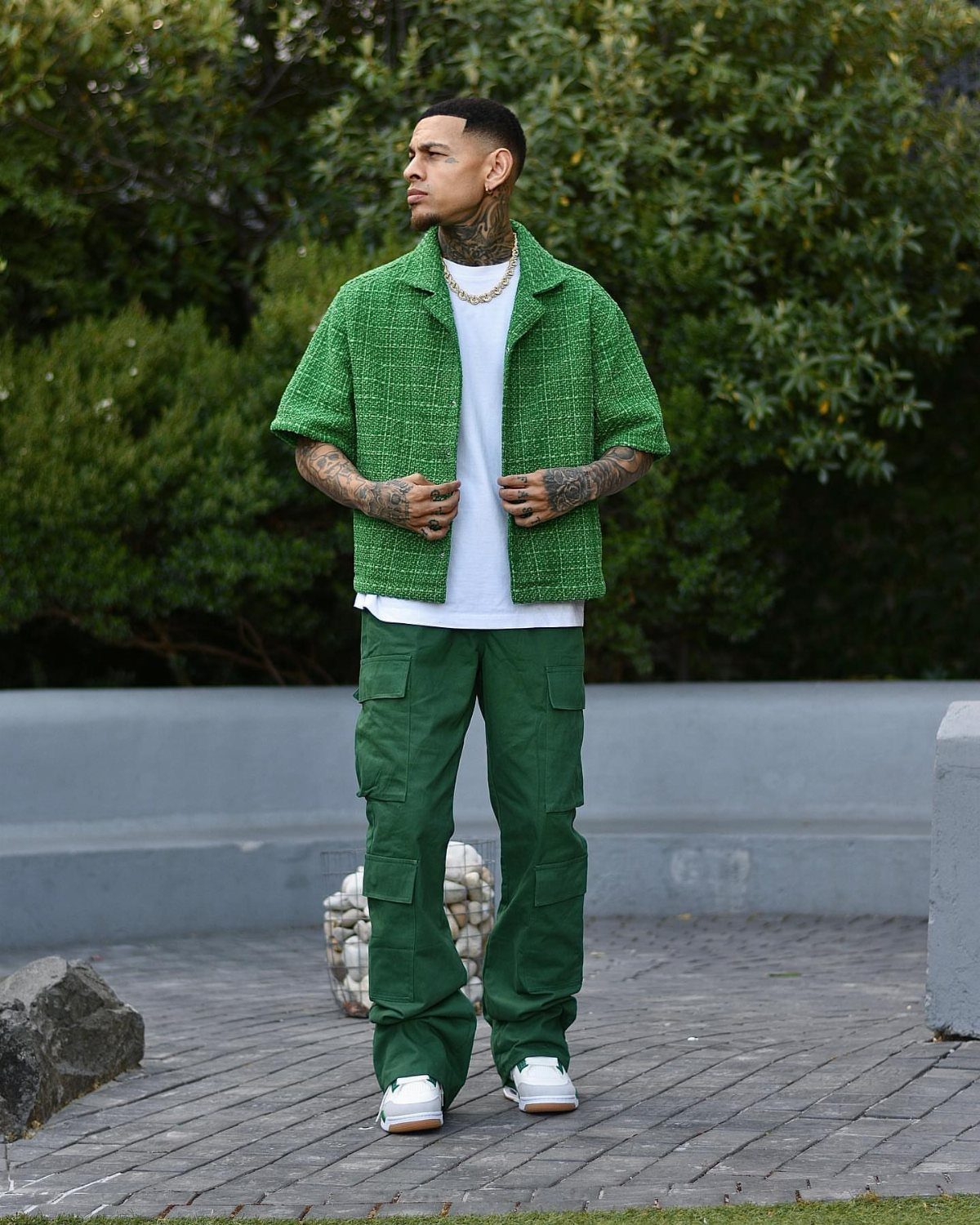 Man wearing a green textured cropped jacket, white t-shirt, and green cargo pants outdoors.