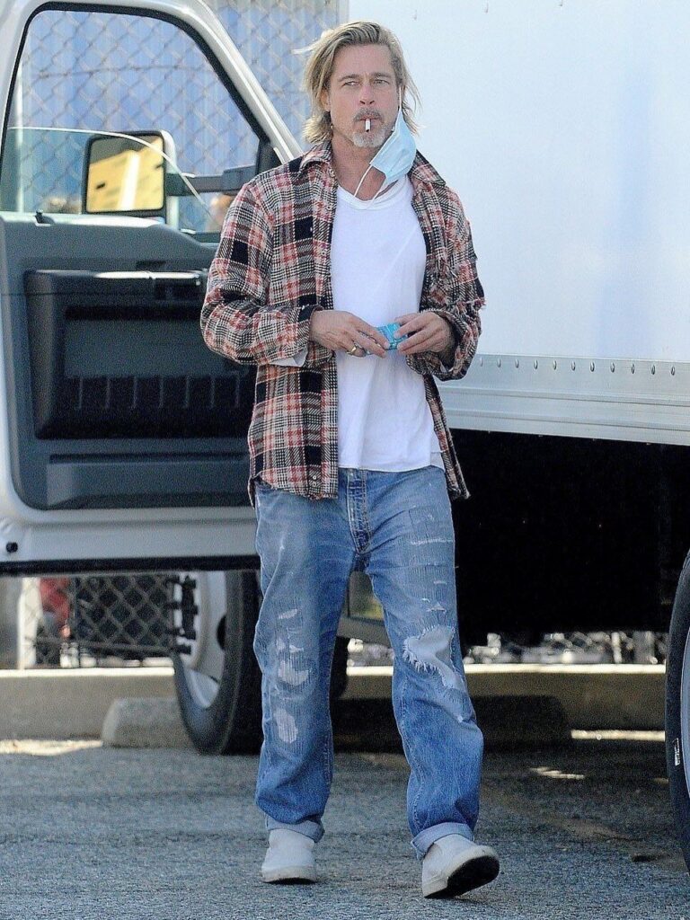 A man walking in a red plaid flannel overshirt, white t-shirt, and distressed blue jeans.