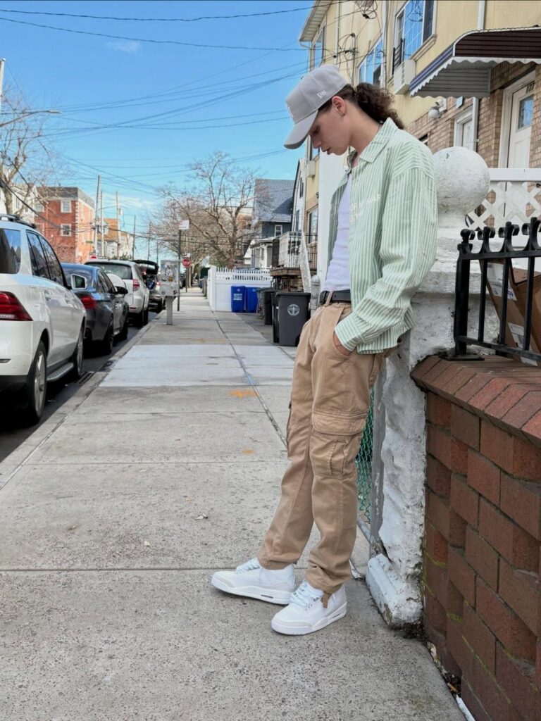 A person wearing khaki cargo pants and a striped button-down shirt standing on a sidewalk.