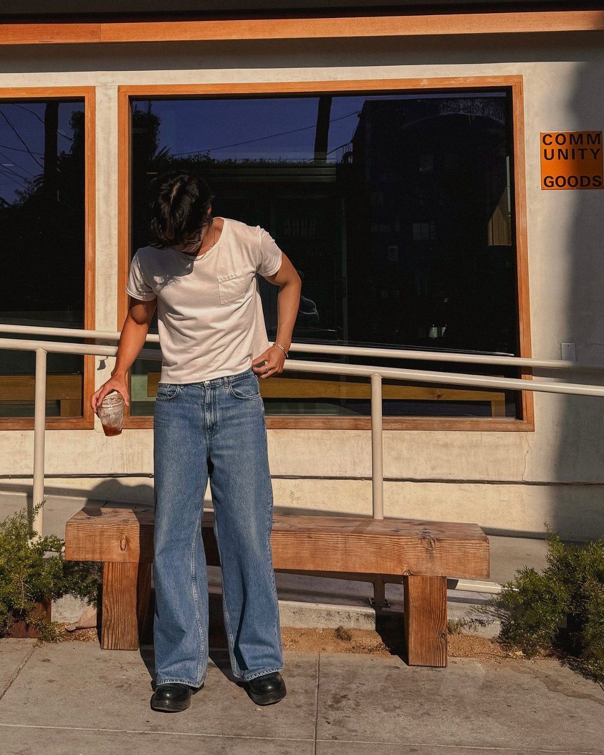 A person wearing a white t-shirt and wide-leg blue jeans standing by a wooden bench.