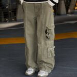 Person wearing a black and white striped top with baggy green cargo pants and white sneakers.