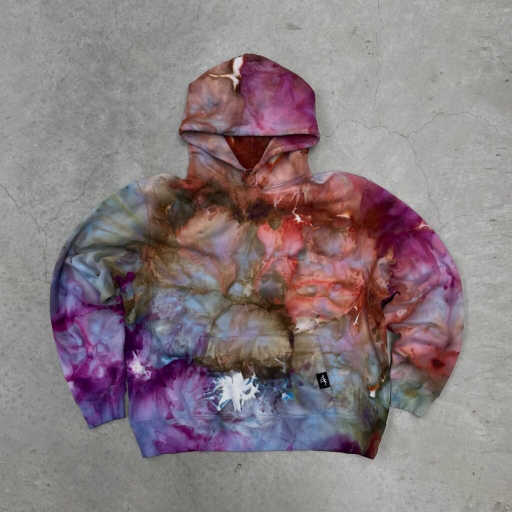 A colorful tie-dye hoodie with purple and blue swirls lying on a concrete floor.