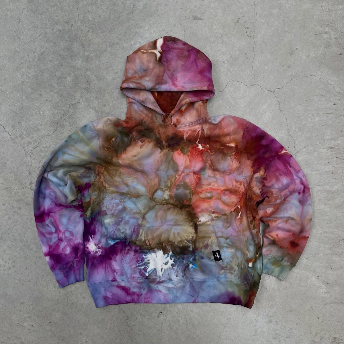 A colorful tie-dye hoodie with purple and blue swirls lying on a concrete floor.