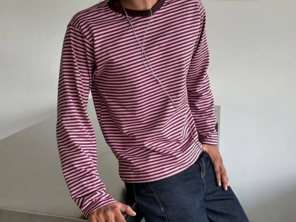 Man wearing a maroon and pink striped long-sleeved tee and dark denim jeans.