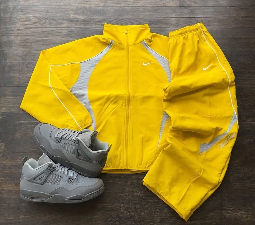 Yellow Nike zip-up jacket and matching track pants with grey sneakers on wood.